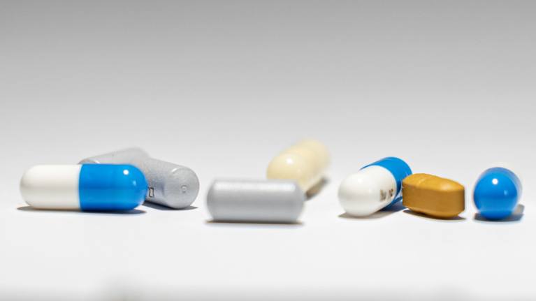 Close-up of 8 different colored pills and tablets on a white surface. 